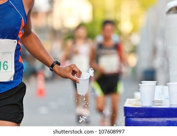 Marathon runner picking up pure water at drinking service point while running in a run race events. Hand of athlete catching up a glass of drink for refreshing during competition.