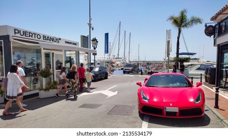 Marbella Malaga Spain June 12 2021. A red Ferrari parked in the harbor area in Puerto Banus. People walking in the Puerto Banus marina. many luxury boats in the background. Colorful luxury car.