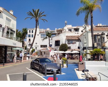 Marbella Malaga Spain June 12 2021. A luxury car parked on the street in the famous Puerto Banus outside Marbella. High palm trees in the small city. People walking on the street in the background.