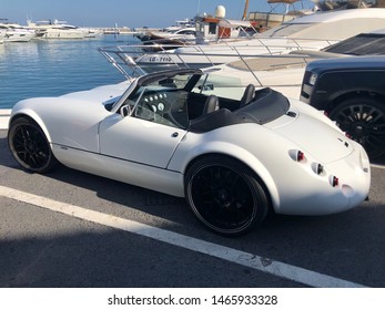 Marbella, Spain - 07 29 2019: original luxury white sport car brand parked alongside other luxury car and several yachts  in marina of Puerto Jose Banus, Spain
