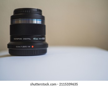 Marbella, Spain- January 04, 2022: A Olympus 45mm f 1.8 fixed focus prime lens on a white table. Olympus rebrands its brand as OM System