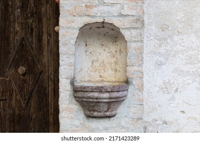 Marble basin for holy water, next to the ancient door. Holy water stoup obtained in a niche in the old wall of an ancient church.