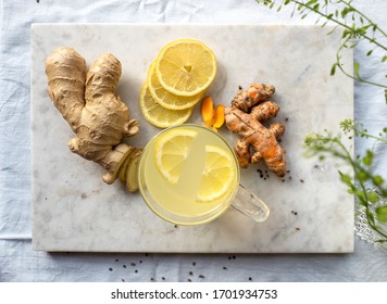 Marble board with immune system boosting ginger, lemon and turmeric hot tea on a set table. 