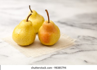 Marble Countertop. Kitchen Counter Top Made Of Classic White Carrera Marble. Three Fresh Yellow Pears On A Burlap Square. Close Up View Of Details And Texture. Copy Space.