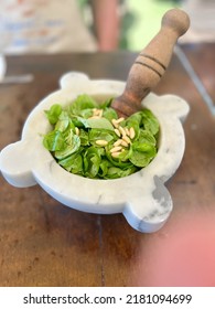 Marble mortar and wooden pestle with basil and pine nuts in preparation of making pesto