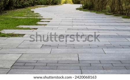 Marble path paved with stone and square tiles. The pedestrian path is paved with paving stones. Grass grows between the tiles. Sidewalk in landscape garden design made of tiled stone slabs. No one
