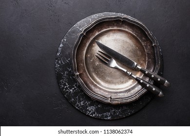 Marble stand and empty vintage plate with fork and knife on black stone background. Top view with copy space
