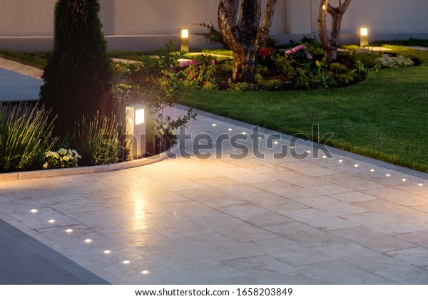 marble tile playground in the night backyard\
of mansion with flowerbeds and lawn with ground lamp and lighting\
in the warm light at dusk in the\
evening.