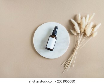 Marble White Round Podium, Amber Cosmetic Bottle With White Label Mock Up And Bouquet Of Dry Lagurus On Beige Background. Top View. Copy Space