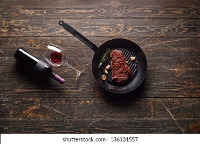 Marbled Beef Steak In A Grill Pan With A Bottle Of Wine And Wine Glass On Old Wood Background. Juicy Food Background.
