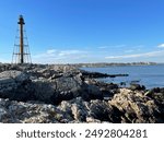 The Marblehead Lighthouse stands on the edge of a rocky coast overlooking a harbor