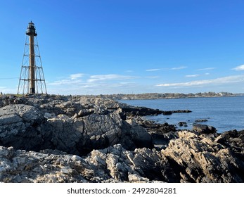 The Marblehead Lighthouse stands on the edge of a rocky coast overlooking a harbor - Powered by Shutterstock