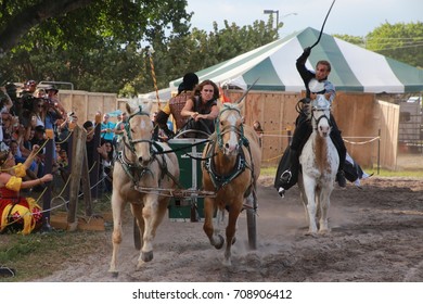 MARCH 18 2017 - RENAISSANCE FESTIVAL - DEERFIELD BEACH, FL  A Warrior Riding Horseback With A Whip Chases Other Warriors In A Horse And Carriage In Front Of Spectators.