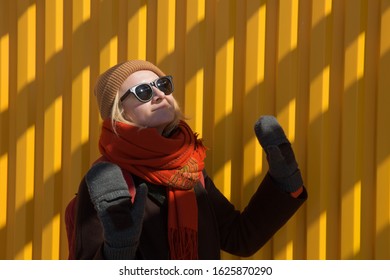 March 2018, New York, United States - a girl wearing winter hat, scarf and brown coat on yellow background with shadow stripes.