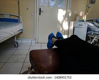 March 2019, Bucharest, Romania Colentina Hospital. Relative Of Patient Has Feet Up On A Chair In Room With Patient. Disposable Polypropylene Shoe Covers. Blue Sterile Shoe Cover/protector For Hospital