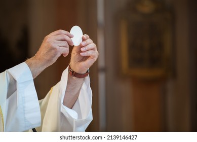 March 2022, Holy host in the hands of the priest on the altar during the celebration of the mass and empty space for text - Shutterstock ID 2139146427