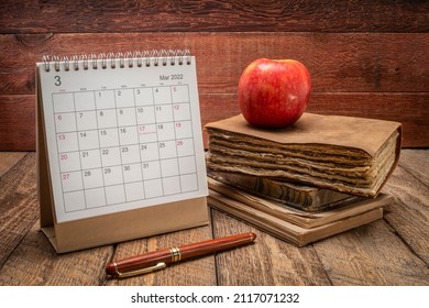 March 2022 - spiral desktop calendar with a stack of old book against rustic wooden background, time and business concept