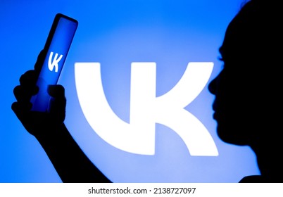 March 25, 2022, Brazil. In this photo illustration, a woman's silhouette holds a smartphone with the VKontakte (VK) logo displayed on the screen and in the background