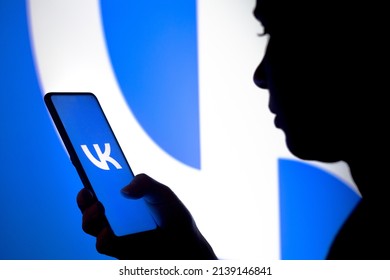 March 26, 2022, Brazil. In this photo, a woman's silhouette holds a smartphone with the VKontakte (VK) logo displayed on the screen and in the background