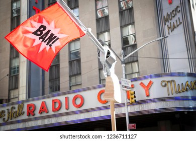 March For Our Lives: A Protester Passing Radio City Music Hall Holds A Sign In The Shape Of A Gun With A Red Flag That Says BAN At The March On 6th Ave To End Gun Violence, NEW YORK MAR 24 2018.