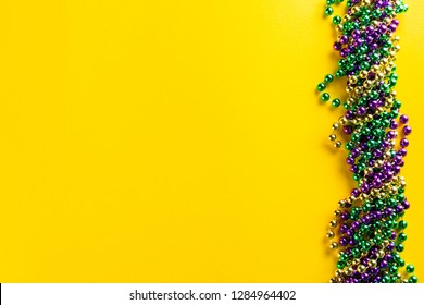 Mardi gras carnival concept - beads on yellow background, top view