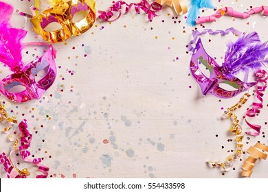 Mardi Gras Or Carnival Frame With Brightly Colored Metallic Foil Masks With Feather Decoration And Twirled Streamers On A Pale Pink Background With Copy Space