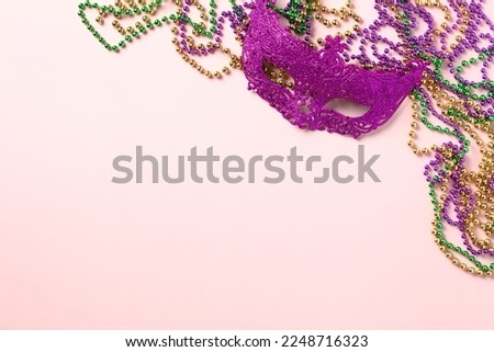 Mardi Gras carnival mask and beads for party on pink background. Flat lay, top view.