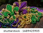 Mardi Gras color beads with fleur de lis on wooden table in sunlight