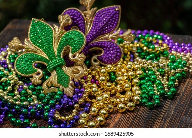 Mardi Gras color beads with fleur de lis on wooden table in sunlight