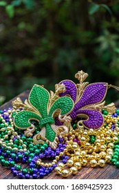 Mardi Gras Color Beads With Fleur De Lis On Wooden Table In Sunlight