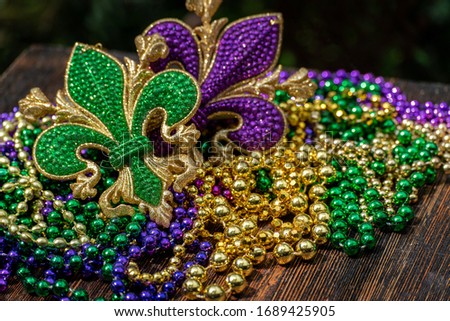 Mardi Gras color beads with fleur de lis on wooden table in sunlight