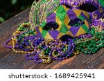 Mardi Gras color beads with masks on wooden table in sunlight