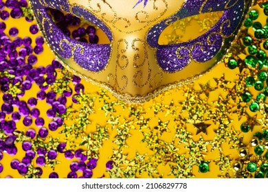 Mardi Gras gold color beads with Luxury Masquerade venetian festival carnival mask and golden, green, purple confetti on yellow background. Party invitation, greeting card,  carnivale celebration time