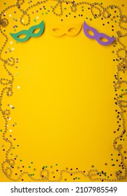Mardi Gras gold color beads with Masquerade festival carnival masks and golden, green, purple confetti on yellow background. Party invitation, greeting card, venetian carnivale celebration concept.