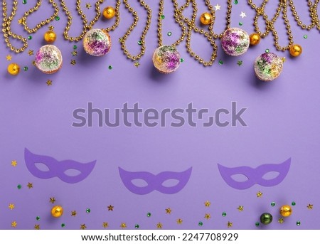 Mardi Gras King Cake cupcake or muffins, masquerade festival carnival mask, gold beads and golden, green confetti on purple background. Holiday party invitation, greeting card concept.