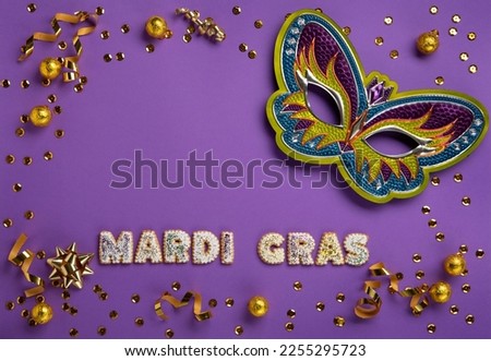 Mardi Gras masquerade festival carnival Mask, chocolate candies in foil, gold beads and golden confetti on purple background. Holiday party invitation, greeting card concept.
