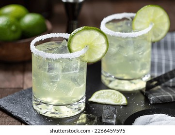 Margarita cocktail with ice, lime slice and salt rim on a black slate board