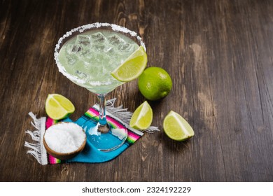 Margarita cocktail with sliced and whole limes on wooden bar table. Mexican party background