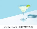 Margarita or Daiquiri cocktail in glass with lime on blue background, top view. Trendy concept of cocktail beach party, summer vacation.