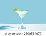 Margarita or Daiquiri cocktail in glass with lime on blue background, copy space. Trendy concept of cocktail party, classic cocktail recipe.