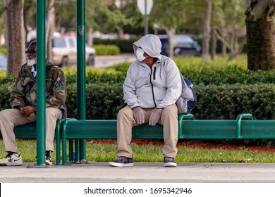 Margate, Florida / USA - 4/3/2020: Man Seated On Green Bench Waiting For Broward Transit Bus Wearing A Medical Grade N95 Surgical Face Mask And Clear Vinyl Latex Protective Gloves Worried Of Covid-19