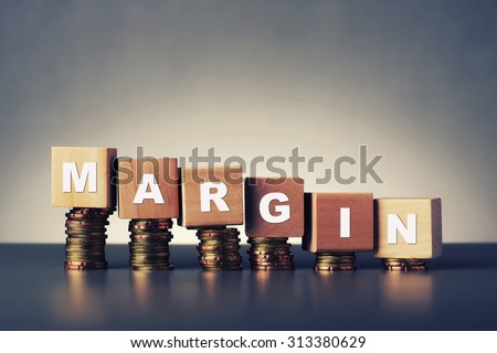 margin text written on wooden block with stacked coins on grey background