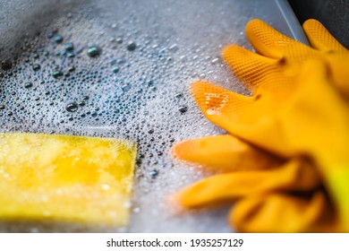 Marigold Washing Up Gloves In A Bowl Of Soapy Water With A Spong. CLose And Selective Focus With Bokeh.