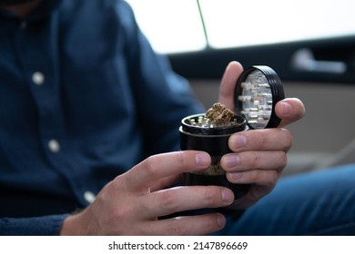 Marijuana Joint In Hand Bud Flowers Of Cannabis. Grinder And Shredded Cannabis Joint Packet Of Weed On A Car Background Close Up