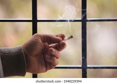 Marijuana Joint Lit, In The Hands, With Prison Gate And Forest In The Background