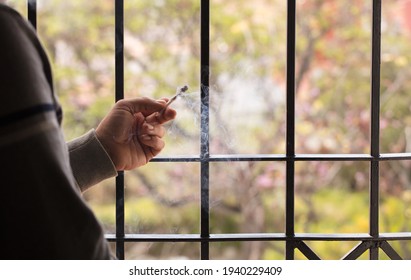 Marijuana Joint Lit, In The Hands, With Prison Gate And Forest In The Background