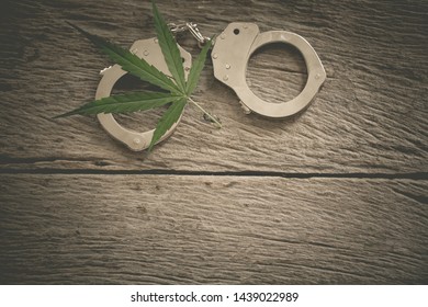 Marijuana Leaf With Iron Handcuffs On The Background Of A Wooden Table. Law Violation