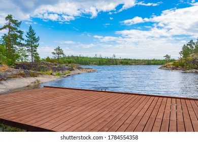 Marina At The Forest Lake. Boat Dock On The Background Of The Lake. Wooden Flooring Against The Background Of Water And Rocky Banks.