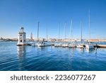 Marina and lighthouse tower on San Giorgio di Maggiore with city of Venice behind. Venezia, Italy, Europe. Sailing boats, yachts moored by pier. Sunshine, daylight, calm sea water with reflections.