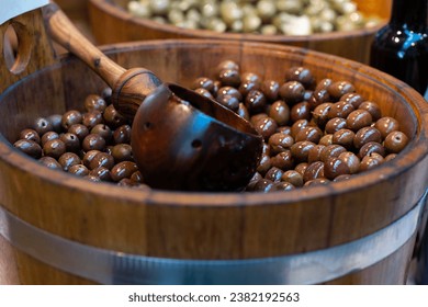 Marinated black olives in a wooden barrel in a market, close-up. - Powered by Shutterstock